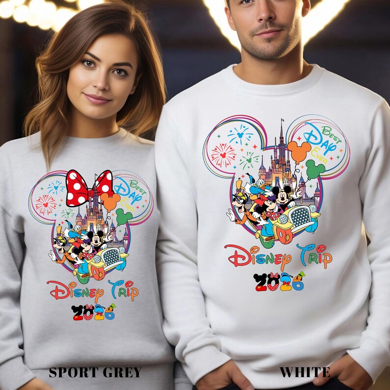 May include: Sport grey and white sweatshirts with a colorful Disney Trip 2020 design. The design features Mickey Mouse, Minnie Mouse, and other Disney characters in a car, with a castle and fireworks.