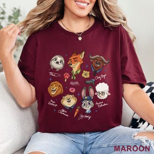 Pu&ograve; includere: T-shirt bordeaux con personaggi dei cartoni animati di Zootropolis, tra cui Flash, Nick Wilde e Judy Hopps. La maglietta presenta i nomi dei personaggi e la scritta MAROON in basso. Un design divertente e colorato per i fan del film d'animazione.