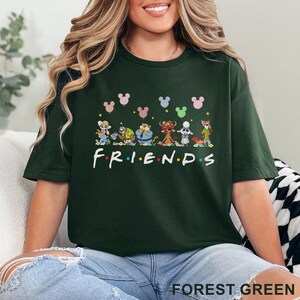 May include: Forest green t-shirt featuring the word "FRIENDS" in white, with cartoon characters and Mickey Mouse head silhouettes above. The shirt is a dark green color.