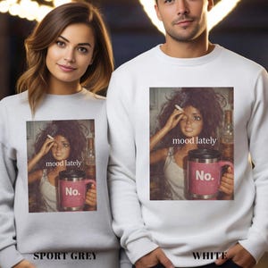 May include: A sport grey sweatshirt and a white sweatshirt, each featuring a graphic print of a doll with messy hair holding a cigarette and a pink mug with the text 'No.' and the caption 'mood lately' printed above the mug.