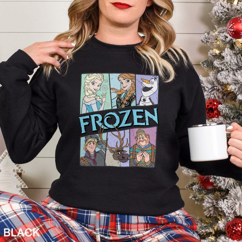 May include: Black crewneck sweatshirt featuring a colorful graphic of characters from the movie "Frozen." The design includes Elsa, Anna, Olaf, Kristoff, Sven, and a character in a green hat. The word "FROZEN" is printed in blue and white. The sweatshirt is worn by a person.