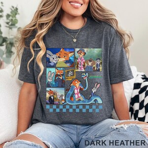 Pu&ograve; includere: T-shirt grigio scuro con una grafica colorata dei personaggi del film d'animazione "Zootopia". Il design include pi&ugrave; pannelli con immagini dei personaggi, con la parola "Zootopia" in verde. Il testo "DARK HEATHER" &egrave; in basso.