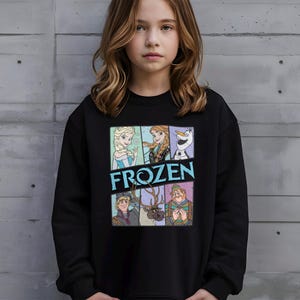 May include: Black crew neck sweatshirt featuring characters from the animated film "Frozen." The graphic includes Elsa, Anna, Olaf, Kristoff, Sven, and Oaken. The word "FROZEN" is printed in a blue and white font.