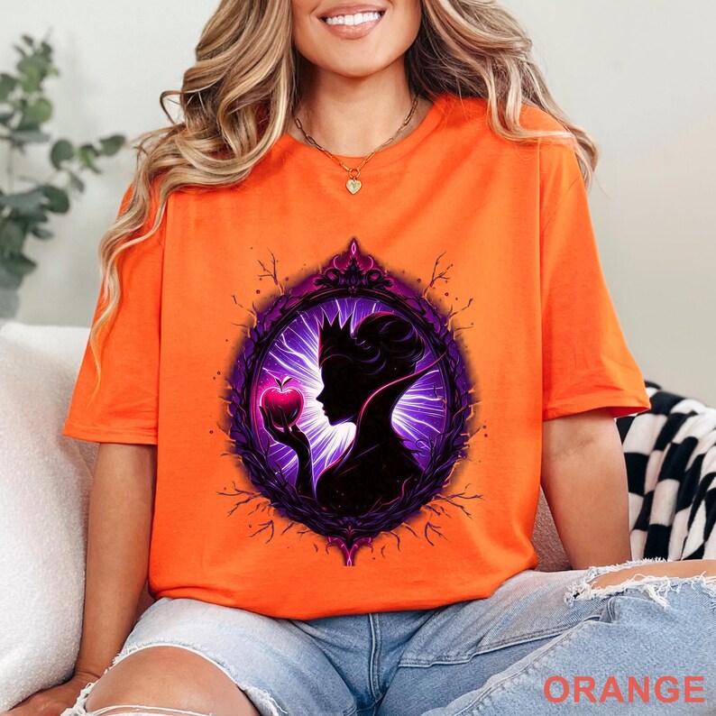 Puede incluir: Camiseta naranja brillante con la silueta de una reina sosteniendo una manzana dentro de un marco decorativo. El dise&ntilde;o es en tonos morados y negros, con la palabra "ORANGE" impresa en la parte inferior.