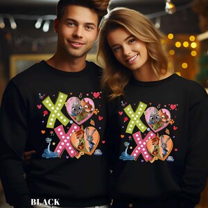 May include: Black sweatshirts featuring a colorful graphic with the text "XO" and heart-shaped illustrations of cartoon characters. The sweatshirts have long sleeves and a crew neck. The word "BLACK" is printed at the bottom.