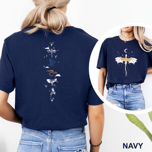 Pu&ograve; includere: T-shirt blu navy con un design a forma di drago. La parte posteriore della maglietta mostra una disposizione verticale di draghi stilizzati in bianco, blu e oro, con stelle. La parte anteriore ha un drago con una luna crescente e stelle.