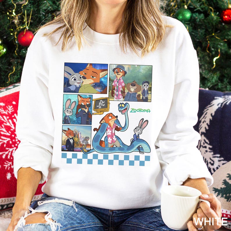 May include: A white long-sleeve sweatshirt featuring a graphic print of various scenes from the movie Zootopia, including characters Nick Wilde and Judy Hopps, with a blue checkered pattern at the bottom and the Zootopia logo in green text.