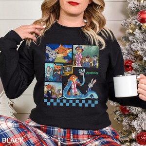 May include: A black long-sleeve sweatshirt featuring a graphic print of various scenes from the movie Zootopia. The design includes multiple panels showing characters like Judy Hopps and Nick Wilde, with the Zootopia logo printed in green.