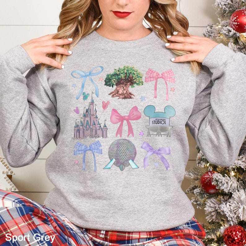 May include: Sport Grey sweatshirt featuring colorful illustrations of bows, a castle, a tree, and other theme park icons. The design includes the word "Studios" and a Mickey Mouse head. The sweatshirt is a comfortable, casual style.