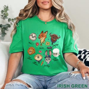 Pu&ograve; includere: T-shirt verde irlandese con personaggi dei cartoni animati di Zootopia. Il design include Nick Wilde, Judy Hopps e altri personaggi. Il testo "IRISH GREEN" si trova in basso a destra sulla maglietta.
