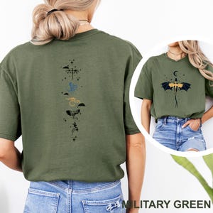 Pu&ograve; includere: T-shirt verde militare con un disegno di drago. La parte posteriore della maglietta mostra una disposizione verticale di draghi stilizzati in vari colori. La parte anteriore della maglietta mostra un drago con una luna crescente e stelle.