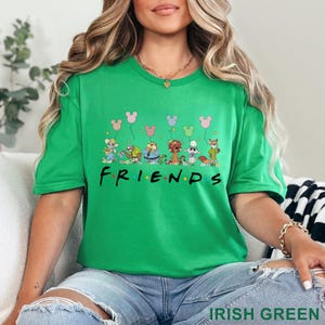 May include: Irish green t-shirt featuring a cartoon design of animal characters holding Mickey Mouse balloons. The word "FRIENDS" is printed in black. The shirt is made of a soft material.