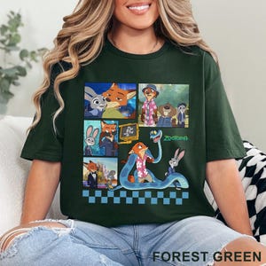 Pu&ograve; includere: T-shirt verde foresta con un collage di personaggi dei cartoni animati di Zootopia. Il design include immagini di Nick Wilde, Judy Hopps e altri personaggi del film d'animazione. La parola "Zootopia" &egrave; stampata in verde.