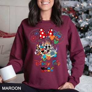 May include: Maroon sweatshirt featuring a colorful Disney Trip design. The graphic includes Mickey Mouse, Minnie Mouse, and other characters in a car, with the text "Best Day Ever" and "Disney Trip 2023". A large red bow with white polka dots is at the top.