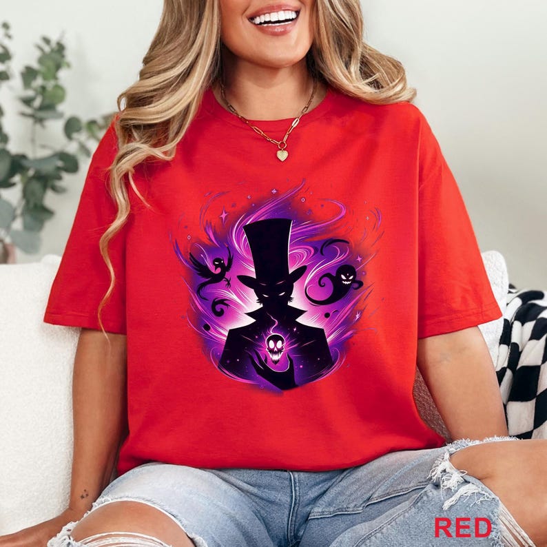 Puede incluir: Camiseta roja con un gr&aacute;fico de una figura silueteada con sombrero de copa, sosteniendo una calavera brillante, rodeada de energ&iacute;a p&uacute;rpura y figuras fantasmales flotantes. La palabra "RED" est&aacute; impresa en la parte inferior.