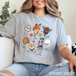 Pu&ograve; includere: T-shirt grigio sportivo con una grafica colorata dei personaggi del film d'animazione Zootropolis. Il design include Flash, Nick Wilde, Capo Bogo, Judy Hopps e altri. Il testo "SPORT GREY" &egrave; stampato in basso.