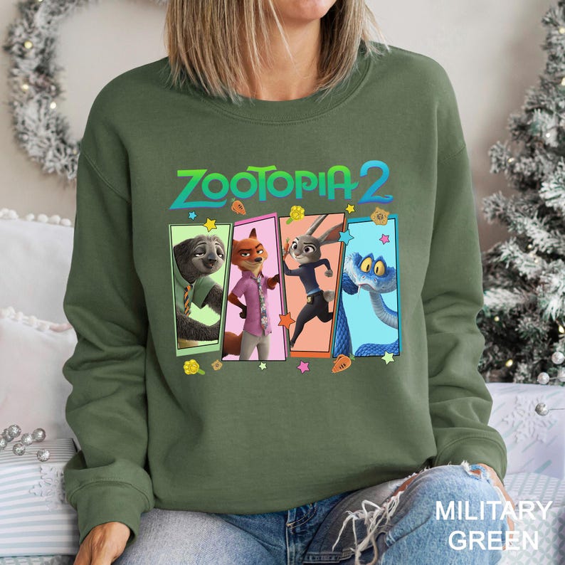 Peut inclure: Sweat-shirt vert militaire avec le texte "ZOOTOPIA 2" au-dessus de quatre panneaux de personnages. Les panneaux affichent un paresseux, un renard, un lapin et un serpent. Le sweat-shirt est de style d&eacute;contract&eacute;.
