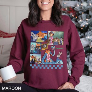 May include: A maroon long-sleeve sweatshirt featuring a graphic print of Zootopia characters including Judy Hopps and Nick Wilde in various scenes, with a blue and white checkered border at the bottom and the Zootopia logo in green text.
