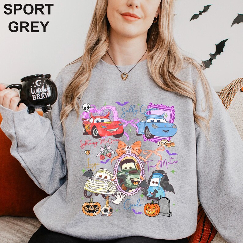 May include: A sport grey crewneck sweatshirt featuring a graphic print of Disney Pixar Cars characters in Halloween costumes, including Lightning McQueen, Sally Carrera, Mater, and Guido, surrounded by pumpkins, bats, and text labels.