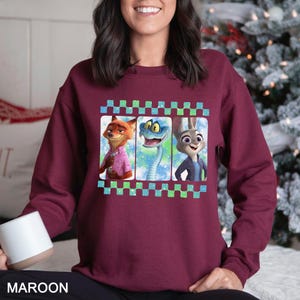 May include: Maroon sweatshirt with a film strip design featuring three cartoon characters: a fox, a snake, and a rabbit. The sweatshirt is a solid maroon colour.