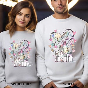 May include: Sport grey and white sweatshirts featuring a colorful castle design with a bow and Mickey Mouse ears. The sweatshirts have the words "SPORT GREY" and "WHITE" printed at the bottom.
