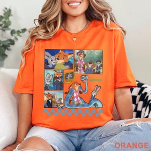 Pu&ograve; includere: T-shirt arancione con una grafica colorata dei personaggi del film d'animazione Zootropolis. Il design include diversi pannelli con varie scene e la scritta "Zootopia". La parola "ORANGE" &egrave; stampata in basso.