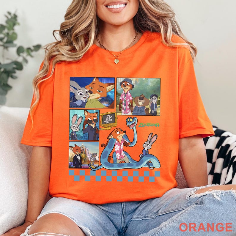 Pu&ograve; includere: T-shirt arancione con una grafica colorata dei personaggi del film d'animazione Zootropolis. Il design include diversi pannelli con varie scene e la scritta "Zootopia". La parola "ORANGE" &egrave; stampata in basso.