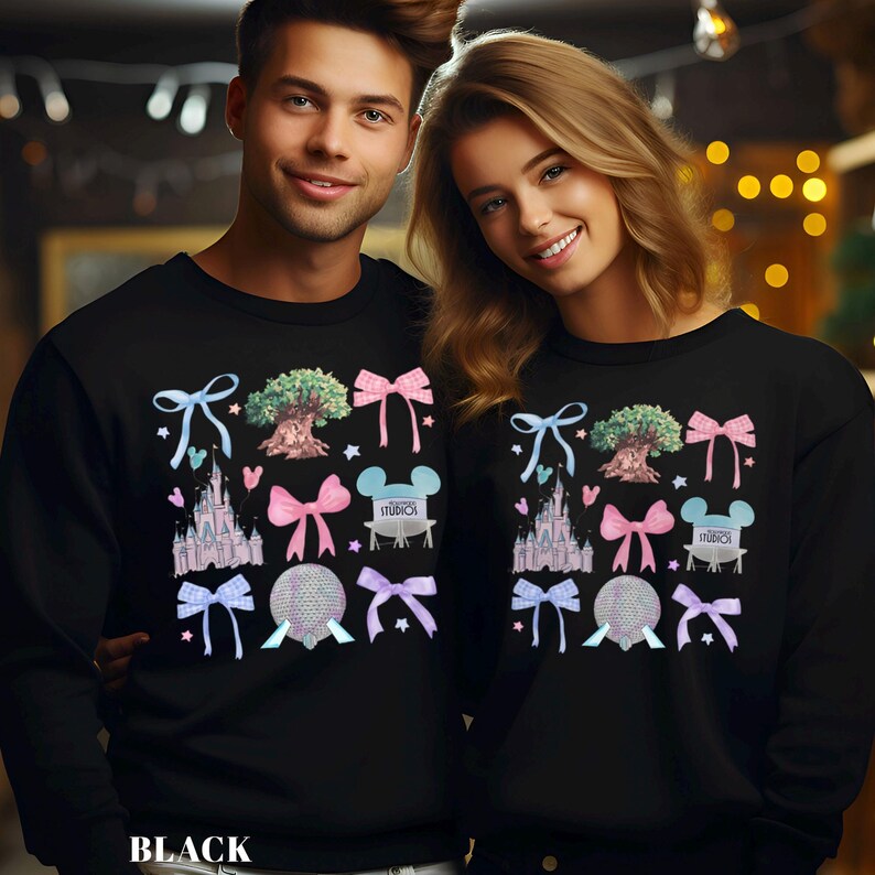 May include: Black sweatshirts featuring a colorful graphic design with a castle, tree, bow, and mouse ears. The word "STUDIOS" is printed on the design. The word "BLACK" is printed at the bottom of the sweatshirt.