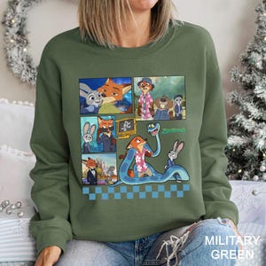 May include: A military green crewneck sweatshirt featuring a graphic print of Zootopia characters including Judy Hopps and Nick Wilde. The design includes multiple panels showing scenes from the movie, a large blue snake, and the Zootopia logo.