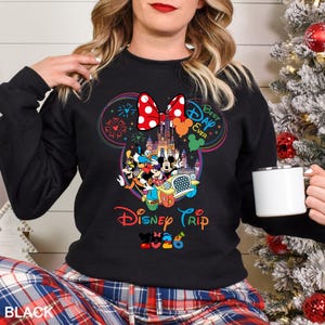 May include: Black sweatshirt featuring a colorful Disney graphic. The design includes Mickey Mouse ears, a polka-dot bow, fireworks, and the words "Best Day Ever" and "Disney Trip 2020". The sweatshirt is worn with plaid pants.