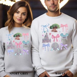 May include: Sport grey and white sweatshirts with colorful graphic designs. The designs include a castle, a tree, bows, and a Mickey Mouse head. The word "STUDIOS" is also visible. The bottom of the sport grey sweatshirt reads "SPORT GREY" and the white sweatshirt reads "WHITE".