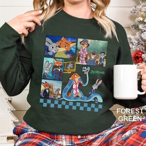 May include: A forest green long-sleeve sweatshirt featuring a graphic print of various scenes from the movie Zootopia, including characters like Nick Wilde and Judy Hopps, with the Zootopia logo and a blue checkered pattern at the bottom hem.