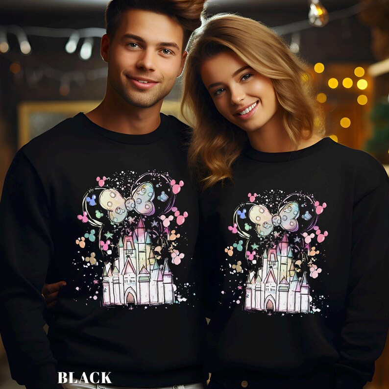 May include: Black sweatshirts featuring a colorful castle design with a bow and Mickey Mouse silhouettes. The sweatshirts have a crew neck and long sleeves. The word "BLACK" is printed at the bottom of the image.