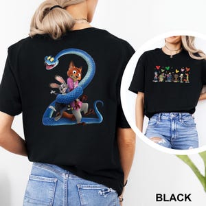K&ouml;nnte beinhalten: Schwarzes T-Shirt mit einem farbenfrohen Aufdruck von Zeichentrickfiguren, darunter eine blaue Schlange, ein Fuchs und ein Kaninchen. Das Design ist vor einem schwarzen Hintergrund platziert. Das T-Shirt wird mit blauen Jeans getragen.