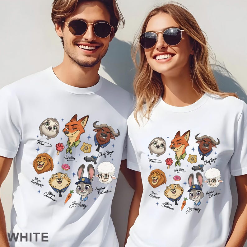 Pu&ograve; includere: T-shirt bianche con una grafica a cartoni animati colorata di personaggi di un film. La grafica include un bradipo, una volpe, un leone, un ghepardo, un coniglio e altri personaggi. La parola "WHITE" &egrave; stampata in basso sulla maglietta.