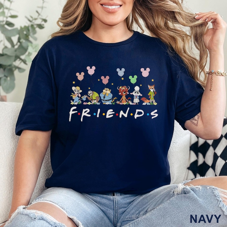 May include: Navy blue t-shirt featuring a cartoon design of Disney characters with Mickey Mouse ears and the word "FRIENDS" in white. The shirt is a casual style, suitable for everyday wear.