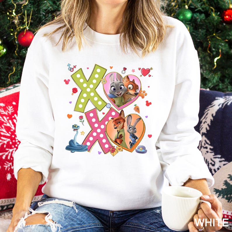May include: White sweatshirt with a colorful graphic featuring the characters Judy Hopps and Nick Wilde from Zootopia. The design includes the letters "XO" with heart and floral accents. The sweatshirt is a casual, everyday wear item.