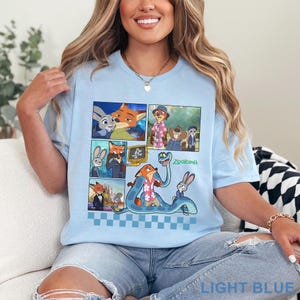 Pu&ograve; includere: T-shirt azzurra con un design a fumetti con personaggi del film d'animazione "Zootropolis". La grafica include immagini di una volpe, un coniglio e altri personaggi. La parola "ZOOTOPIA" &egrave; stampata in verde.