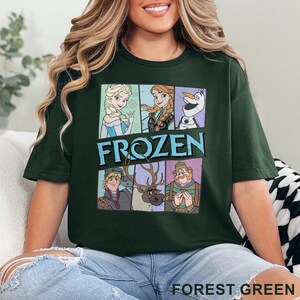 May include: A forest green t-shirt with a graphic print of characters from the animated film Frozen. The characters include Elsa, Anna, Olaf, Kristoff, and Sven. The text "FROZEN" is printed in blue letters.