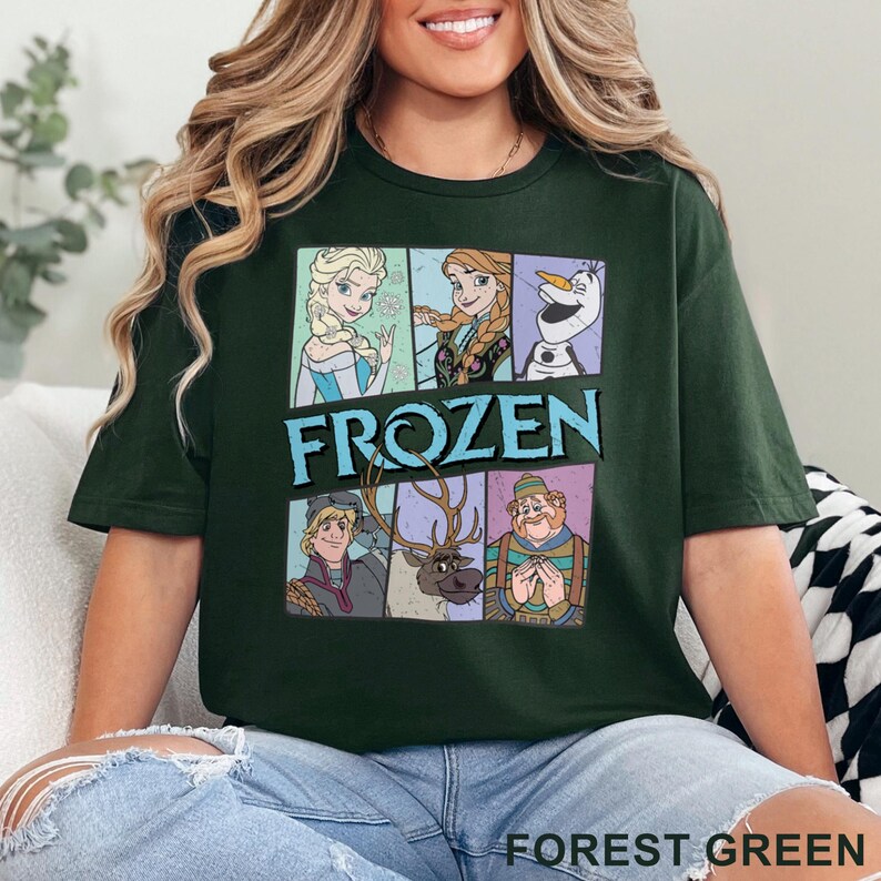 May include: A forest green t-shirt with a graphic print of characters from the animated film Frozen. The characters include Elsa, Anna, Olaf, Kristoff, and Sven. The text "FROZEN" is printed in blue letters.