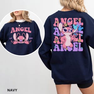 Puede incluir: Sudadera azul marino con un personaje de dibujos animados rosa y la palabra "ANGEL" en rosa. El dise&ntilde;o frontal muestra la cara del personaje y el texto "EST 2004". La parte trasera presenta la palabra "ANGEL" con el personaje y detalles florales.
