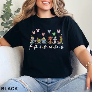May include: Black t-shirt featuring the word "FRIENDS" in white, with cartoon characters and Mickey Mouse-shaped balloons above. The shirt has a crew neck and short sleeves. The word "BLACK" is printed at the bottom of the image.