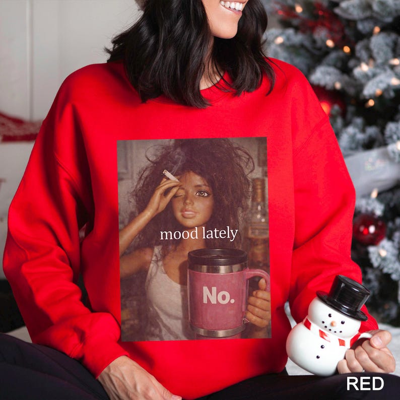 May include: A bright red crewneck sweatshirt featuring a graphic print of a doll with messy hair holding a cigarette and a pink travel mug with the text No. The text mood lately is printed above the mug on the graphic.