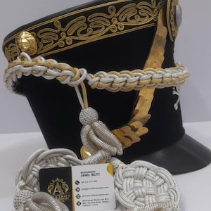 May include: A black military hat with gold and silver decorative trim. The hat features a gold emblem and a silver and gold braided cord. A business card with contact information is visible.