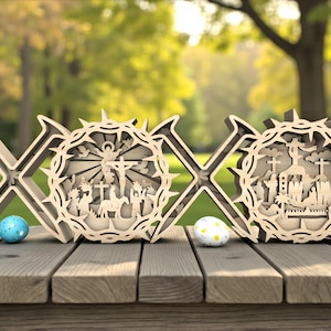 Puede incluir: Decoraciones de Pascua de madera con las letras X y O, con intrincados diseños recortados que representan escenas religiosas. Dos huevos de Pascua decorativos están colocados sobre una mesa de madera. El fondo es un parque verde borroso.