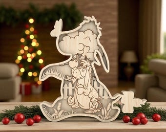 May include: Wooden layered decoration featuring Eeyore from Winnie the Pooh. The light-colored wood carving depicts Eeyore sitting, with a fence, clouds, and grass details. The decoration is placed on a wooden surface with red berries and greenery.