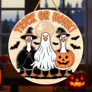 May include: Round wooden Halloween sign with the text "TRICK OR HONK!" featuring three geese in costumes: a witch, a ghost, and a jack-o'-lantern. Bats and a full moon are also included in the design. The sign is hanging by a rope.