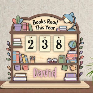 Puede incluir: Decoración de madera con forma de estantería con el texto "Books Read This Year" y el número "238". La decoración incluye una lámpara, un globo terráqueo y el nombre "David". También se incluyen libros decorativos y una planta en maceta.