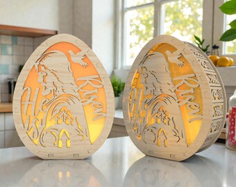 May include: Two wooden Easter egg-shaped lamps with a warm orange glow. The lamps feature a cutout design depicting a religious figure, a dove, and the words "He is Risen." The lamps are made of light-colored wood.