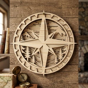 May include: A wooden compass rose wall art piece. The design features a layered mountain and forest scene within the compass star. The piece is made of light-colored wood and is mounted on a wooden wall.
